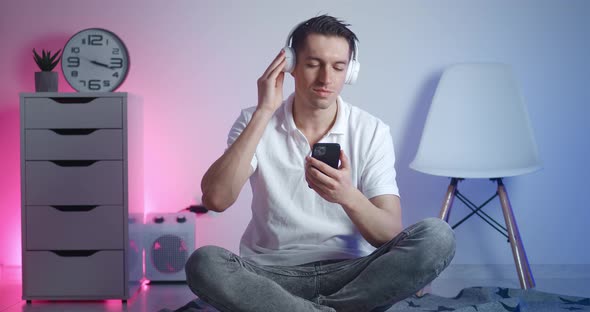 Portrait of Young Stylish Man Enjoying Listening to Music in White Headphones on Smart Phone and