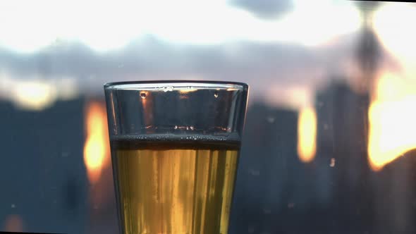 Carbonation bubbles rise in short glass of pale lager beer by window