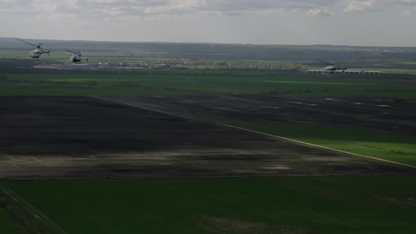 Shooting From the Air Four Helicopters Make a Right Turn in Flight Over Green Fields During the