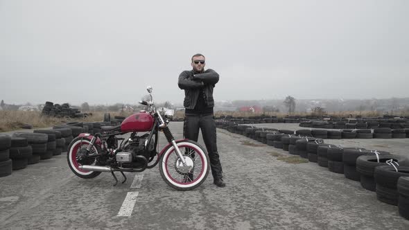 Portrait of Brutal Biker in Sunglasses Crossing Hands and Looking in Distance