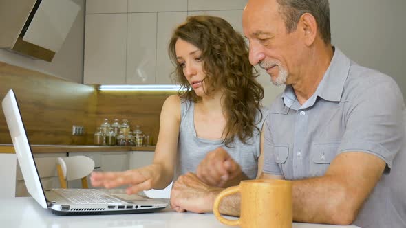 Attractive Young Daughter and Senior Father are Using Laptop Sitting in Modern Kitchen in Apartment