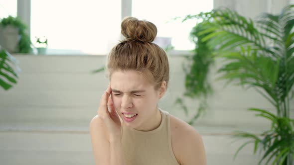 Close Up Nice Young Brunette Woman with Bun on Her Head is Experiencing Severe Headaches