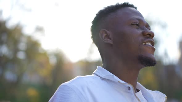 Closeup Side View Face of Positive Handsome African American Man Standing in Sunrays in Autumn Park