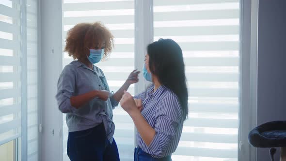 African American and Asian Woman Best Friends with Face Masks Greeting Each Other with Elbow