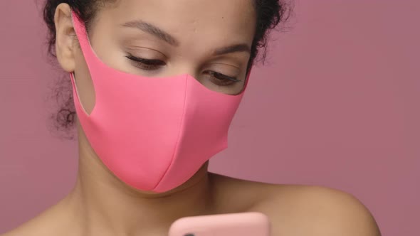 Beauty Portrait of Young African American Woman in Pink Protective Pitta Mask Texting Using