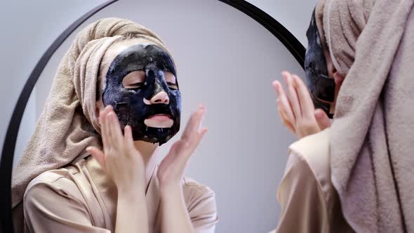 Young woman applying face mask in bathroom and smiling.