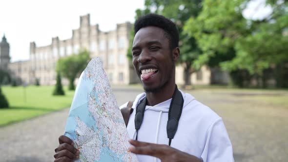 Happy African American Tourist Posing with Paper Map and Binoculars in European Town Outdoors