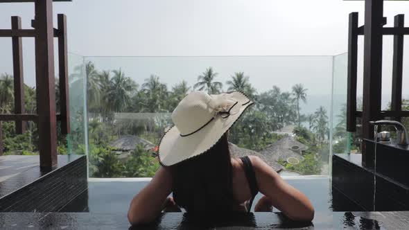 Back view of a female tourist wearing a sun hat and sitting in a open air bath on a balcony or terra