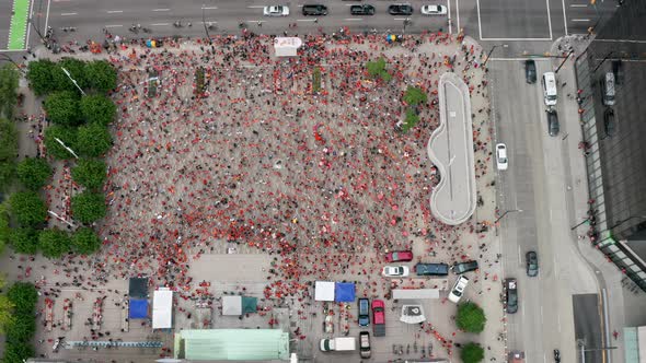 A large group of people in orange shirts gathers in downtown Vancouver, aerial drone slide left. Lot