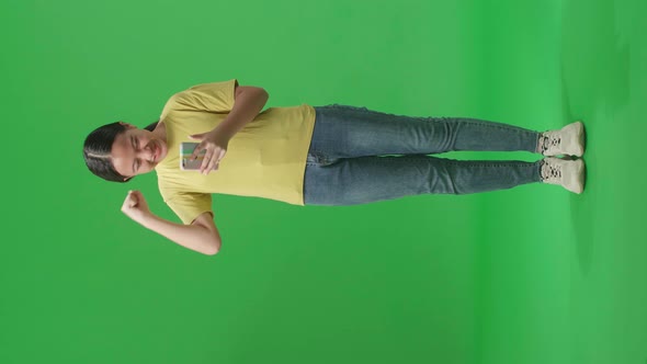 Full Body Of Asian Kid Girl Surprise And Celebrating During Use Phone On Green Screen In The Studio