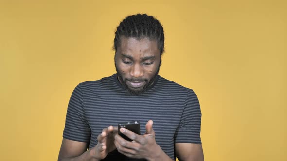 Casual African Man in Shock While Using Smartphone Isolated on Yellow Background