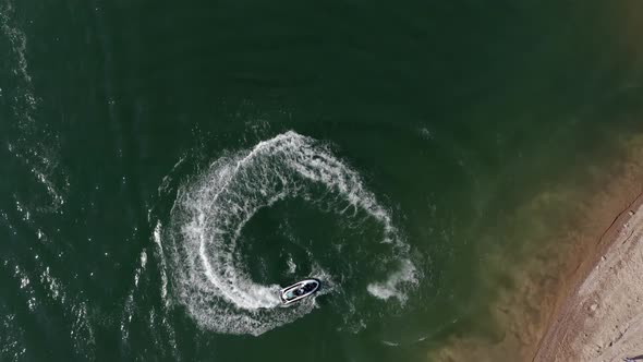 Person on a jet ski turning tight circles near the beach - bird's eye aerial view