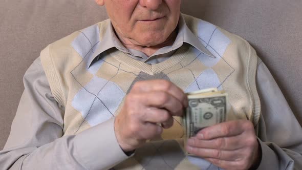 Aged Male Counting Dollars Sitting on Sofa Closeup, Low Living Standard, Subsidy