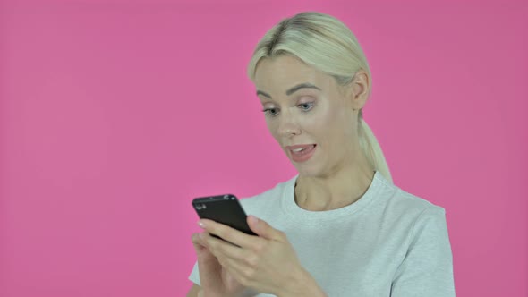 Young Woman Cheering Success on Smartphone, Pink Background