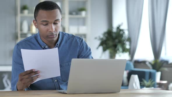 Young African Man Working on Documents and Laptop in Office