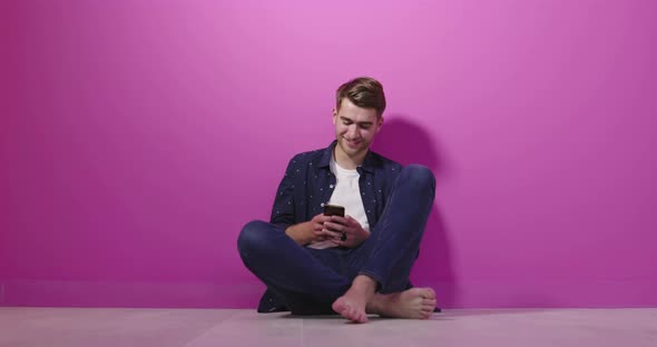 Portrait of a Happy Man Using Mobile Phone Isolated Over Pink Background