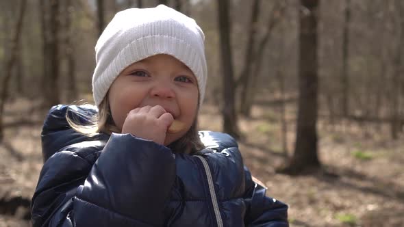 a Little Girl Sits on a Log in the Forest and Eats Delicious Cookies