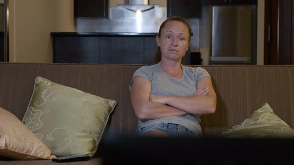 Sad woman watching television sitting on couch at home