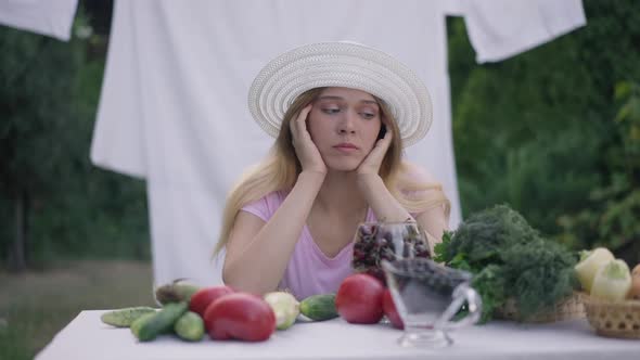 Medium Shot Portrait of Young Sad Woman Sitting in Garden in Front of Table with Vegetables Thinking