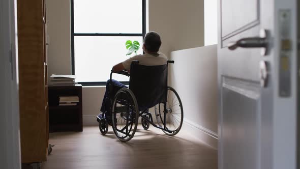 Senior mixed race man in wheelchair wearing face mask and looking through window