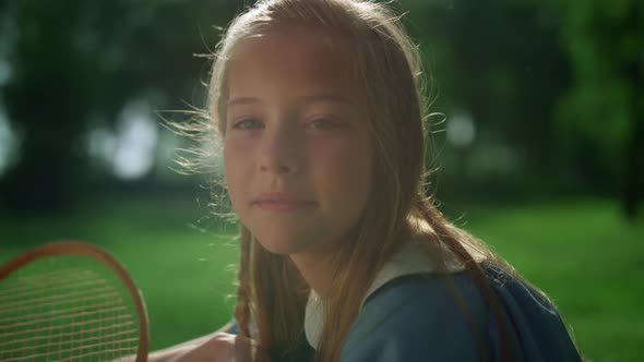 Relaxed Girl Looking Camera Hold Badminton Racket in Green Park Closeup