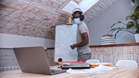 An Online Maths Lesson - an African-american Man Teacher in Medicine Mask and Big Headphones