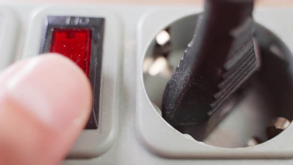 A Finger Presses a Toggle Switch on an Extension Cord with a Red LED Closeup