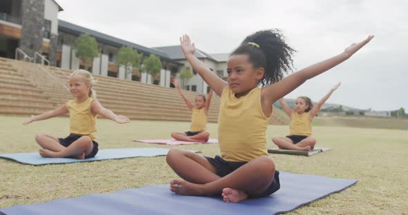 Video of focused diverse girls practicing yoga on mats in front of school