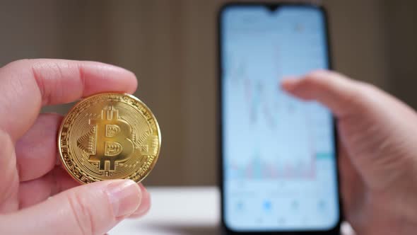 Male Hand Holding Cryptocurrency Coin and Cell Phone Showing Graph