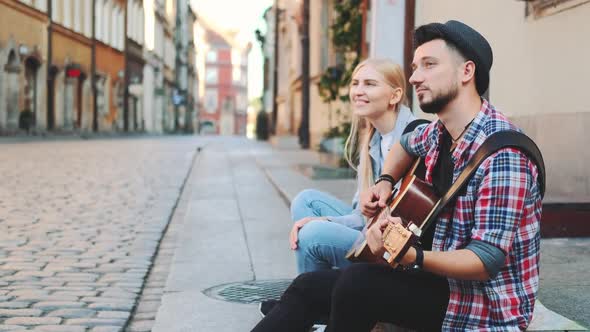 Tourists Sitting on Sidewalk Playing Guitar and Having Rest