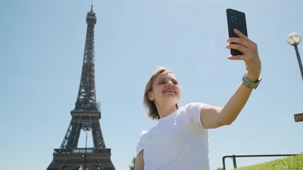 Woman is Taking Selfie Using Smartphone Sitting Near Eiffel Tower in Paris in Daytime Close Up