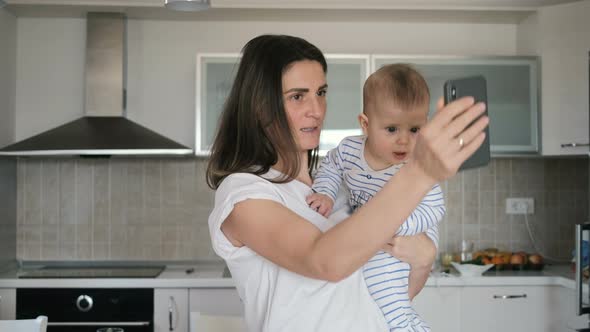 Mother and her baby boy take selfie on a smart phone  in the kitchen at home