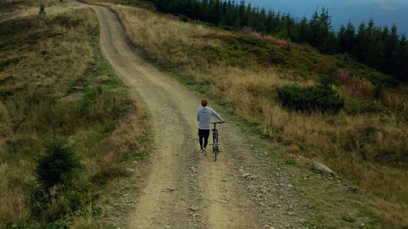 Man Biking Against Mountains Rocky Road Moving Bike Spring Grass Green Trees