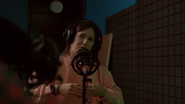 Young woman talking in mic while recording podcast with crop coworker