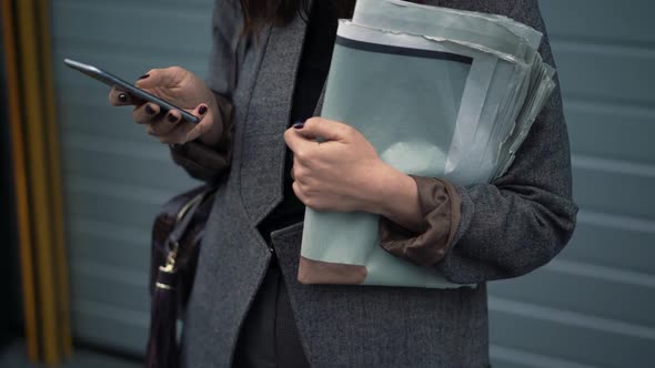 Pan Shot of Woman Holding Newspapers and Typing in the Phone