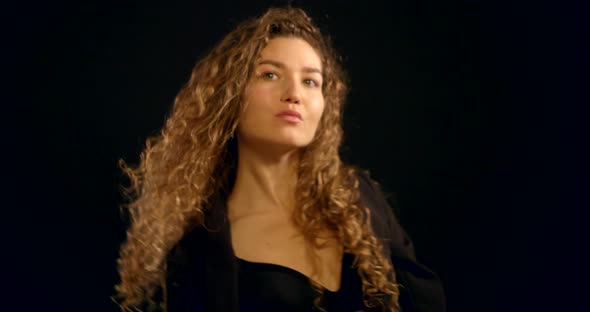 A Close-up Portrait of a Curly-haired Young Girl Who Is in the Studio on a Black Background, Wearing