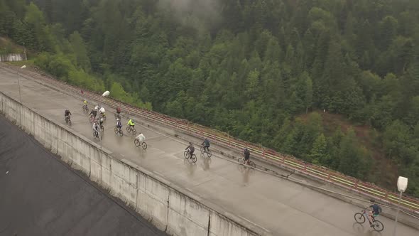 Wide aerial drone shot of mountain bikers crossing a bridge with a forest behind them.