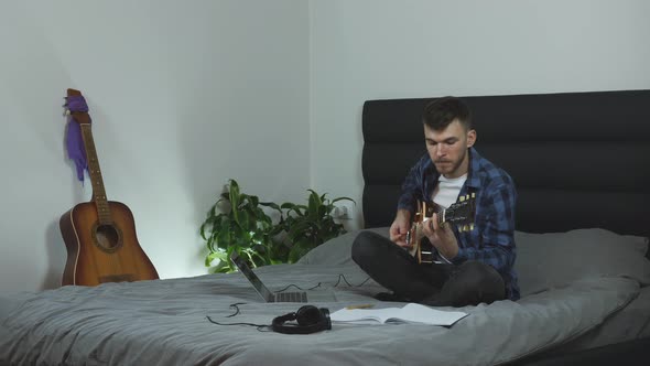 Musician in headphones plays on electric guitar on bed at home, Music concept