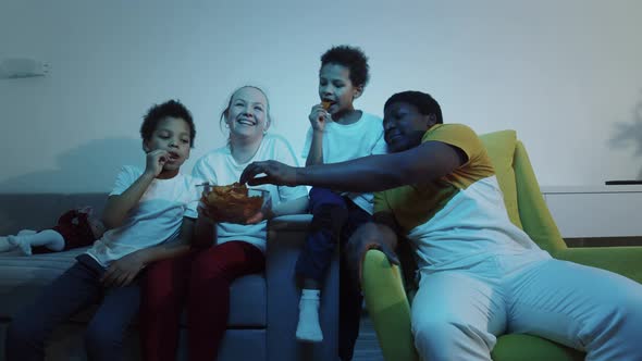 Multirace Family Watching TV and Eating Snacks at Evening