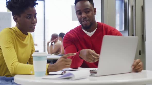 African american male and female business colleagues talking and using laptop in office