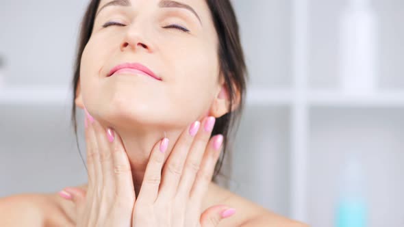 Attractive Smiling Adult Woman Applying Antiaging Cream on Neck and Contour of Chin Closeup