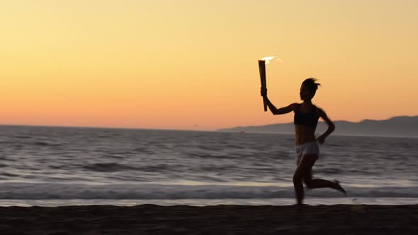 Woman running with a simulated Olympics torch on the beach at sunset.