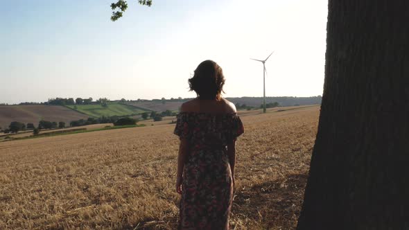 Woman glazes at a wind turbine in the countryside.