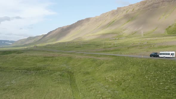 Vehicle Drives At The Narrow Road Amidst The Green Meadow Near The Rugged Mountain In Westfjords, Ic