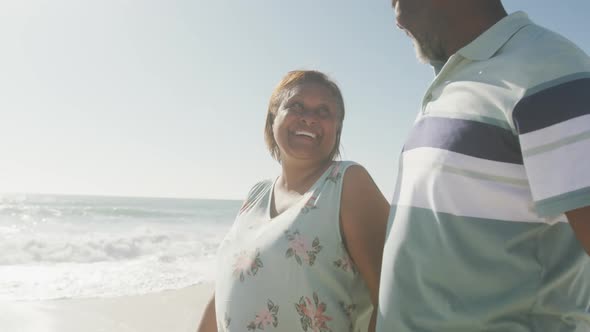 Smiling senior african american couple embracing and walking on sunny beach