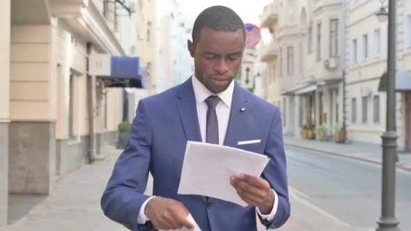 Walking African Businessman Reading Document on the Street