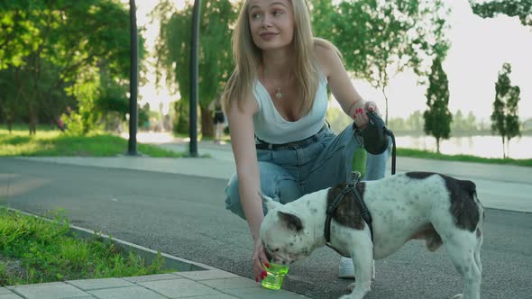 Young Woman Giving Water To Dog in Park.