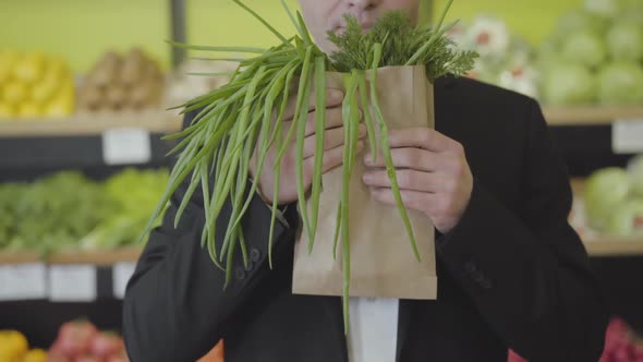 Unrecognizable Caucasian Man Smelling Dill and Green Onion in Paper Pack and Stretching Bunch of