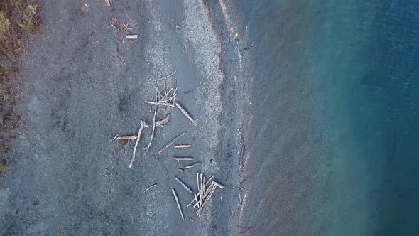 The shoreline of a lake with clear blue water. Rising aerial top down view