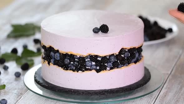 Confectioner decorates a beautiful cake with blueberries and blackberries